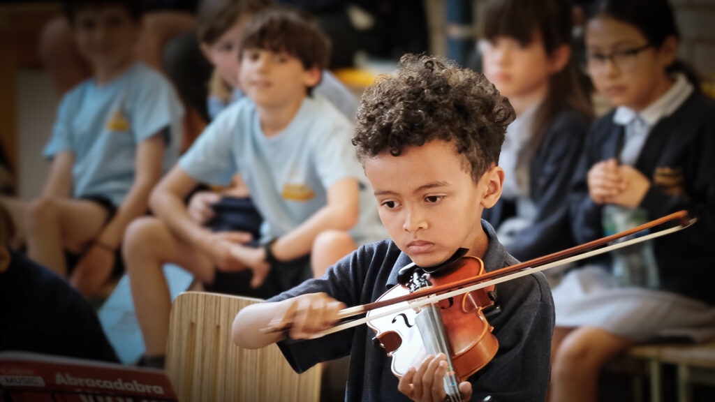 Focused young violin student with audience in background performing in a small school concert