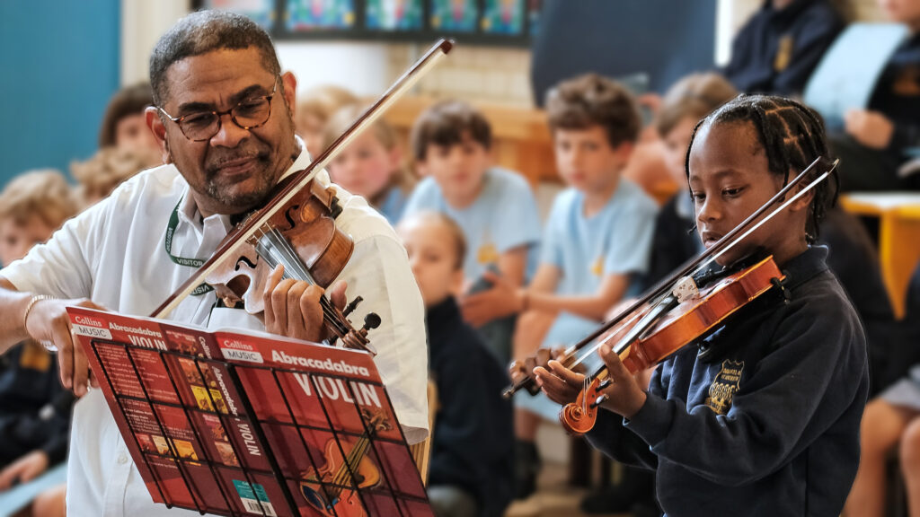 Focused violin student with his teacher performing in a school concert